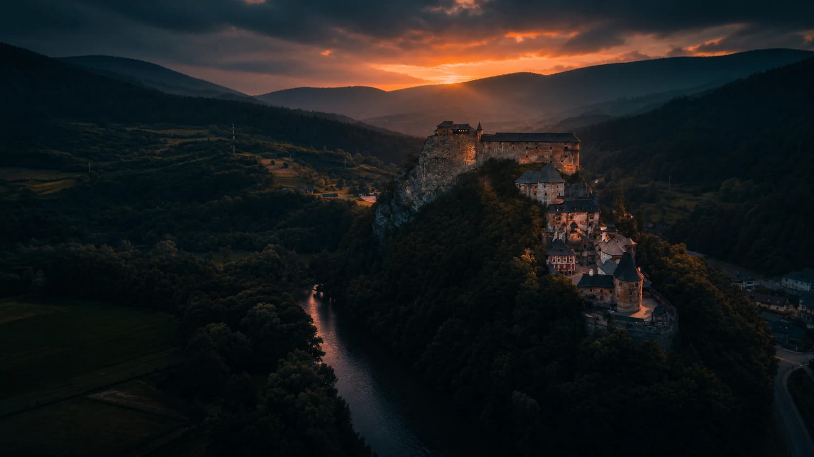 Grad na skalnem pomolu nad gozdnato dolino v večerni svetlobi